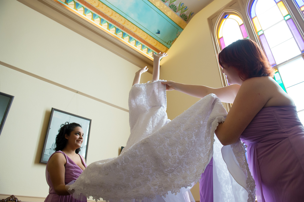 bride's arms peek out of the top of the wedding dress as her bridesmaids help her get dressed