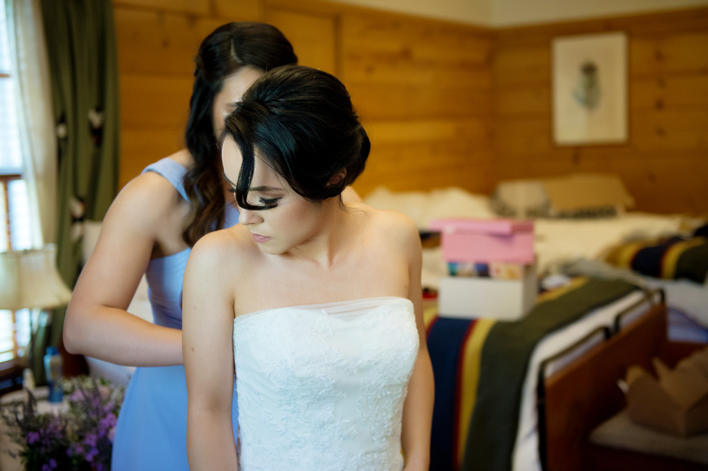 bridesmaid helps bride into wedding dress