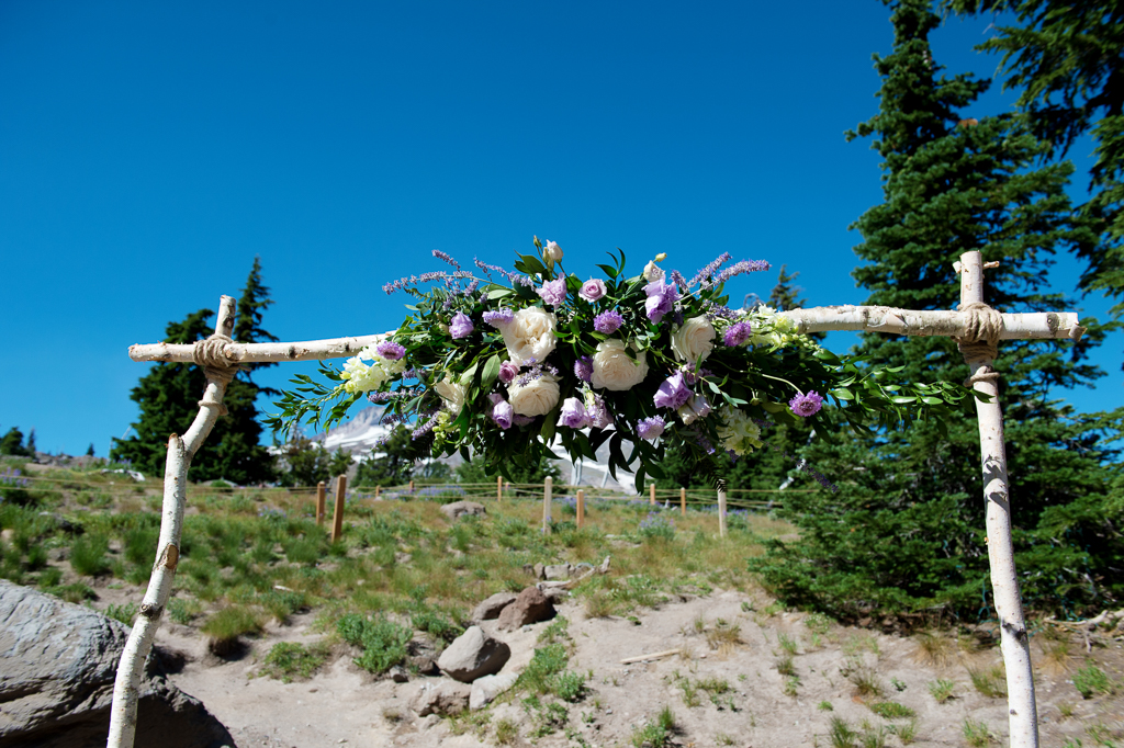 the wedding ceremony arbor covered with purple and white flowers in front of mount hood at timberline lodge