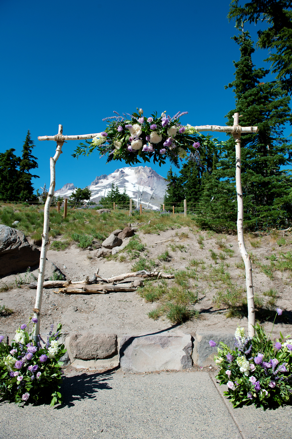 the wedding ceremony arbor covered with purple and white flowers in front of mount hood at timberline lodge