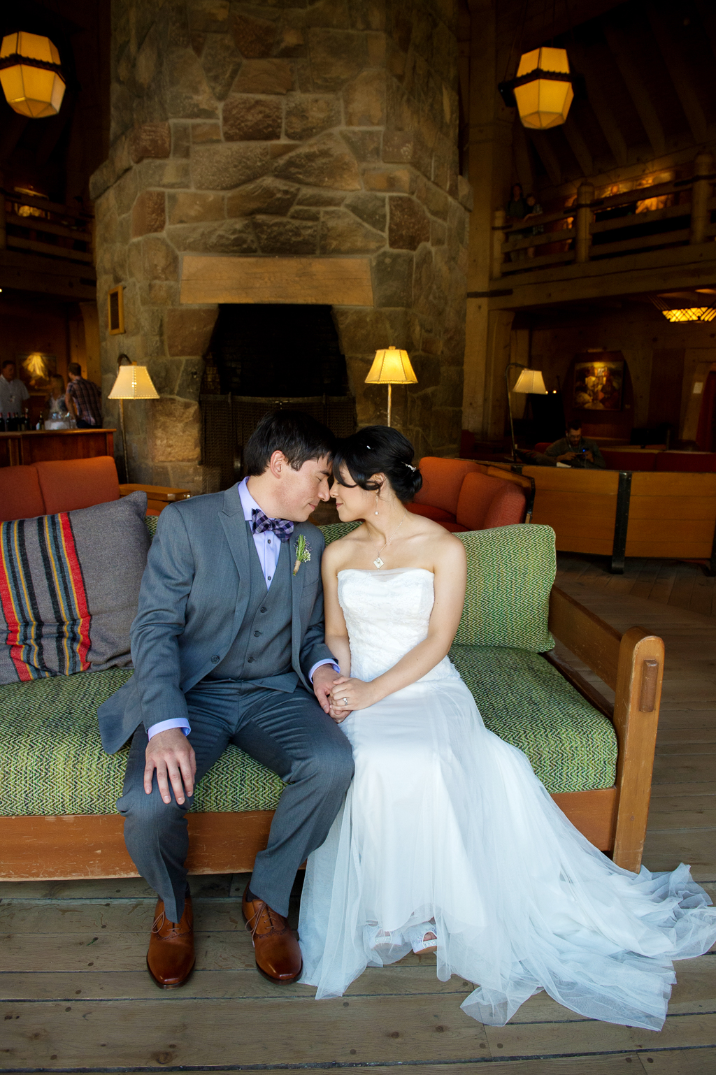 bride and groom sit on green wooden couch in the lodge at timberline