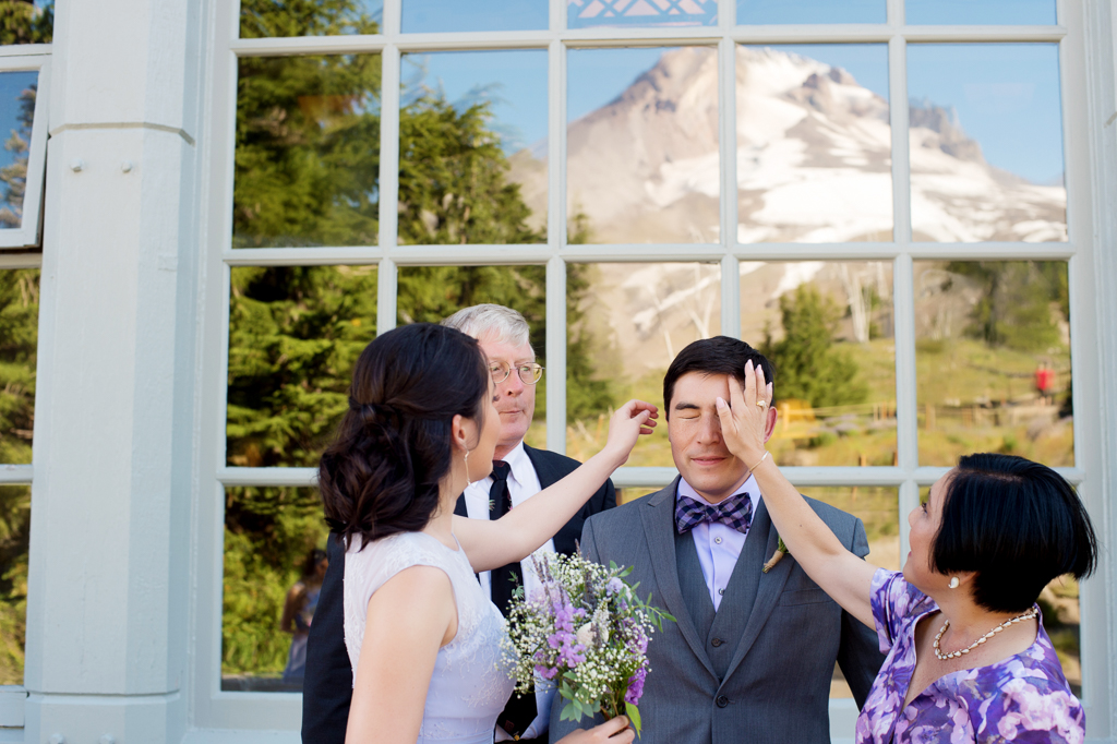 a mom and sister fix a groom's hair with a reflection of mount hood in the window behind them
