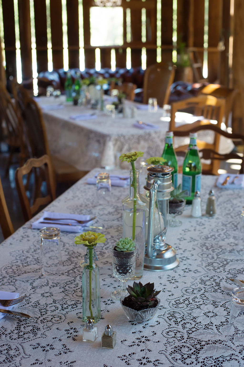 flowers in small glass bottles line the lace covered table at a wedding reception