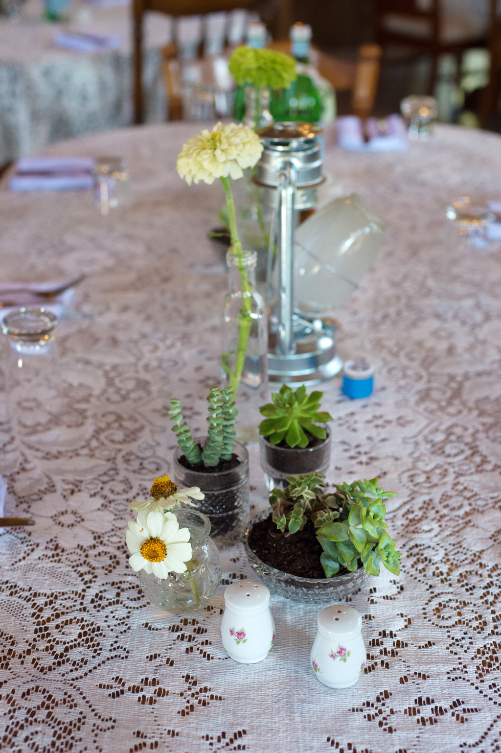 flowers in small glass bottles line the lace covered table at a wedding reception