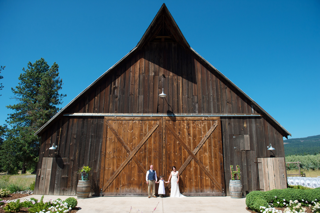 bride groom and daughter hold hands in front of the tin roof barn