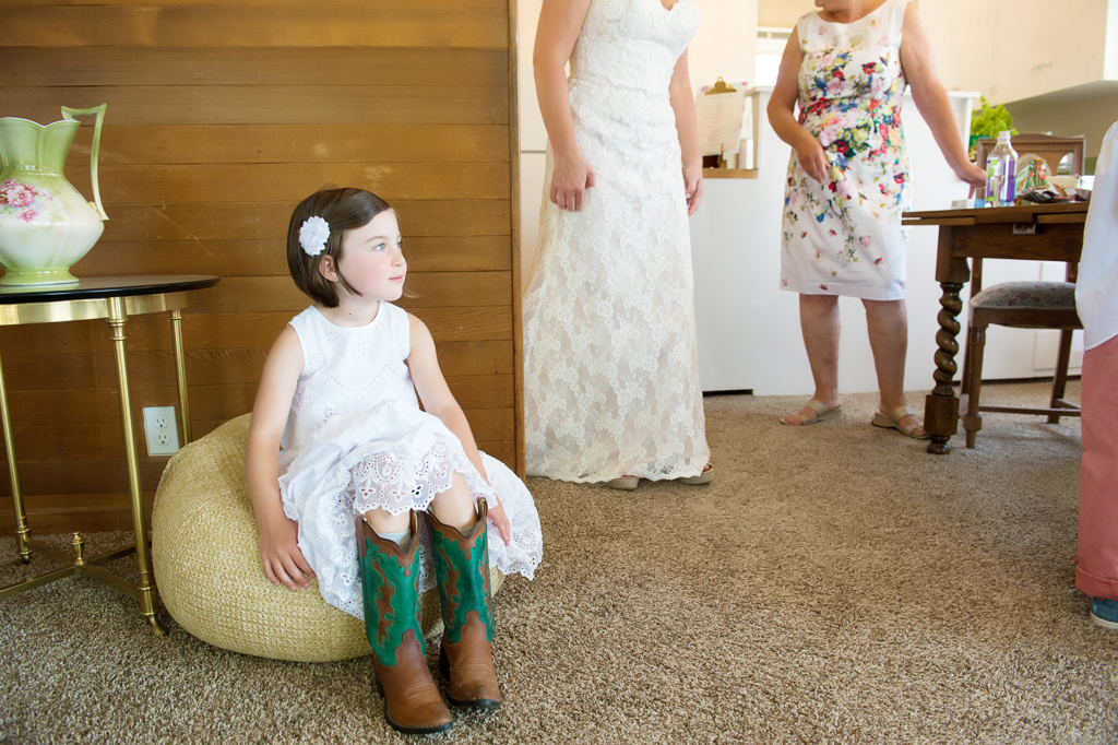 flower girl wearing green and brown cowboy boots sits on a pillow
