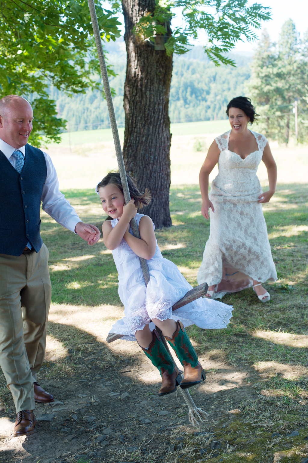 bride and groom push the flower girl on a wooden rope swing