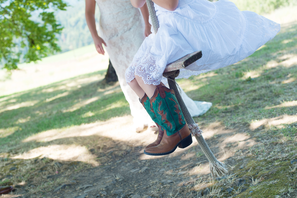flower girl wears green and brown cowboy boots and she swings from a tree swing