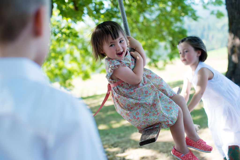 a little girl in a floral calico dress smiles as she swings from a tree