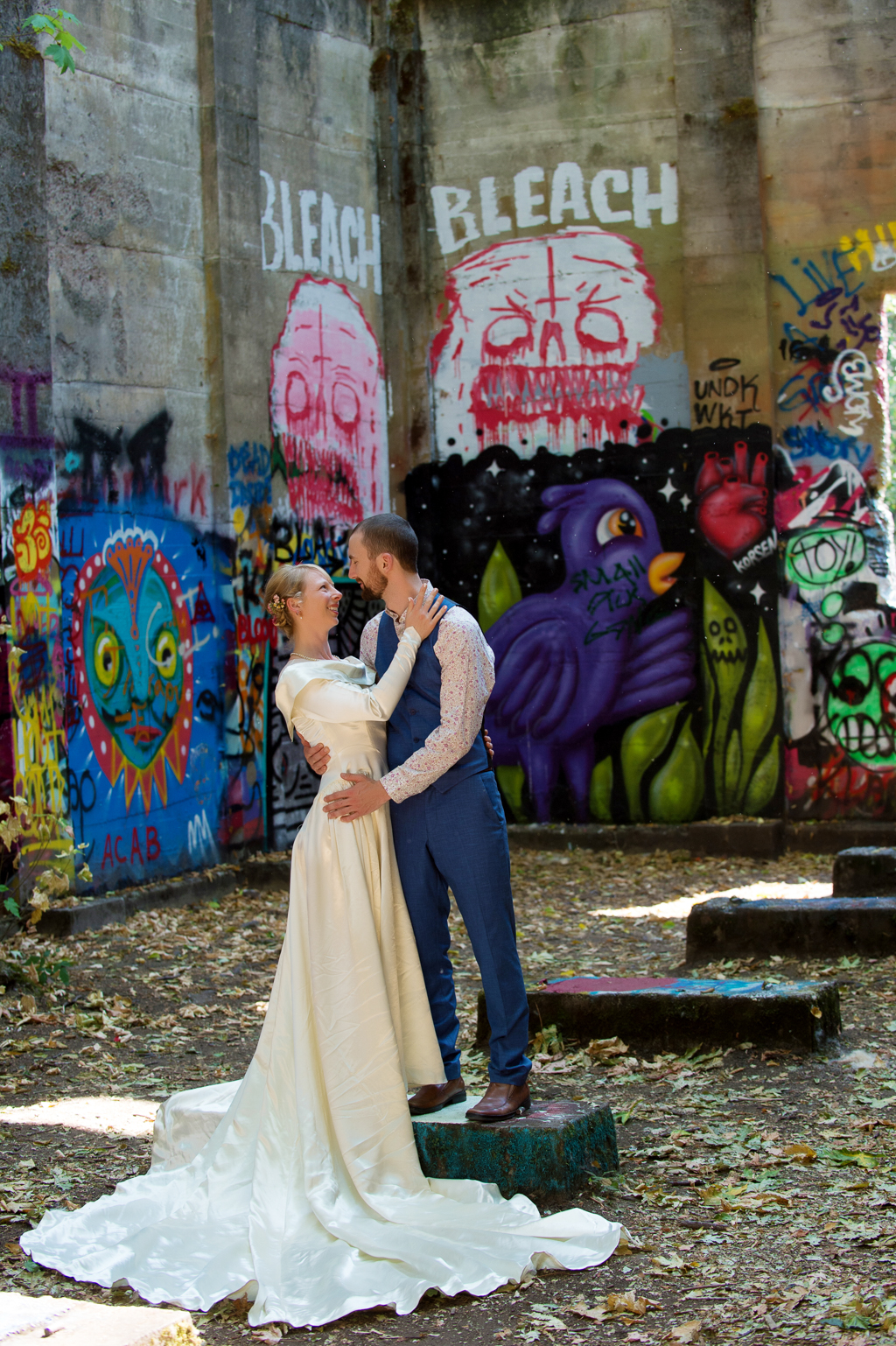 A bride and groom look at each other in a graffiti covered mill