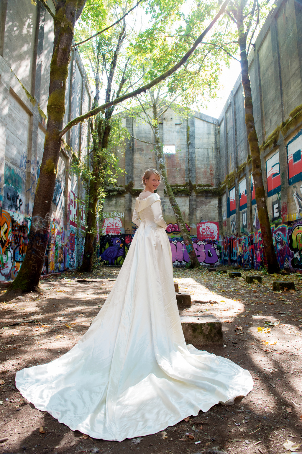 a bride wears a long sleeved vintage wedding dress with a huge train in an old mill covered in graffiti