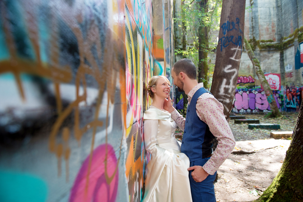 bride leans against graffiti covered wall as groom caresses her cheek