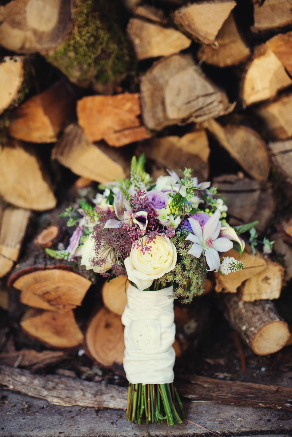 a pretty purple and lilac bouquet sits in front of a pile of chopped wood