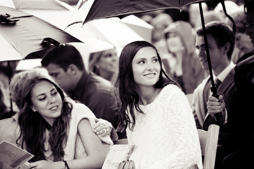guests under umbrellas turn to watch the bride walk down the aisle