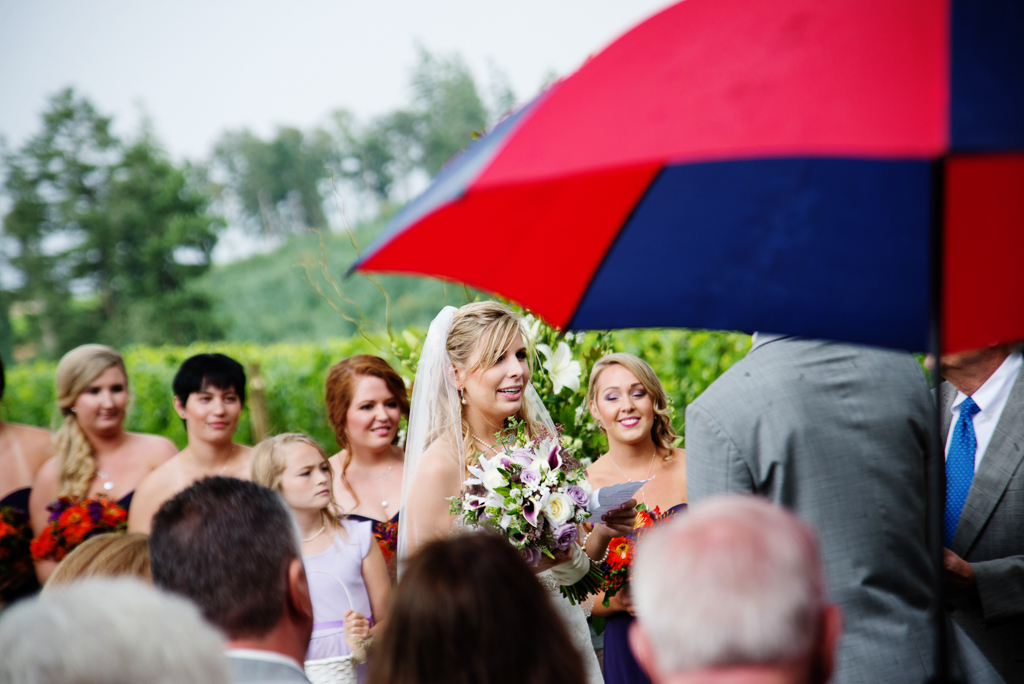 the bride says her vows while guests holding umbrellas watch