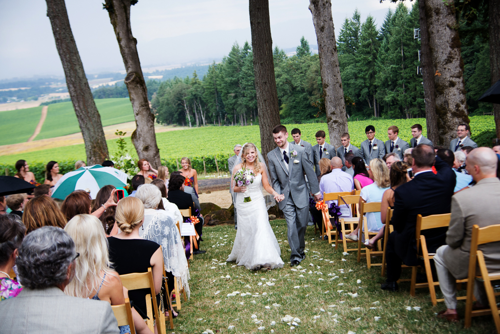 a bride and groom hold hands and exit the ceremony with vista hills vineyard in the background