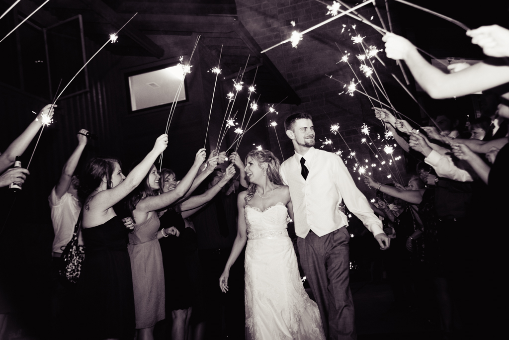 a bride and groom exit their wedding reception while guests hold sparklers