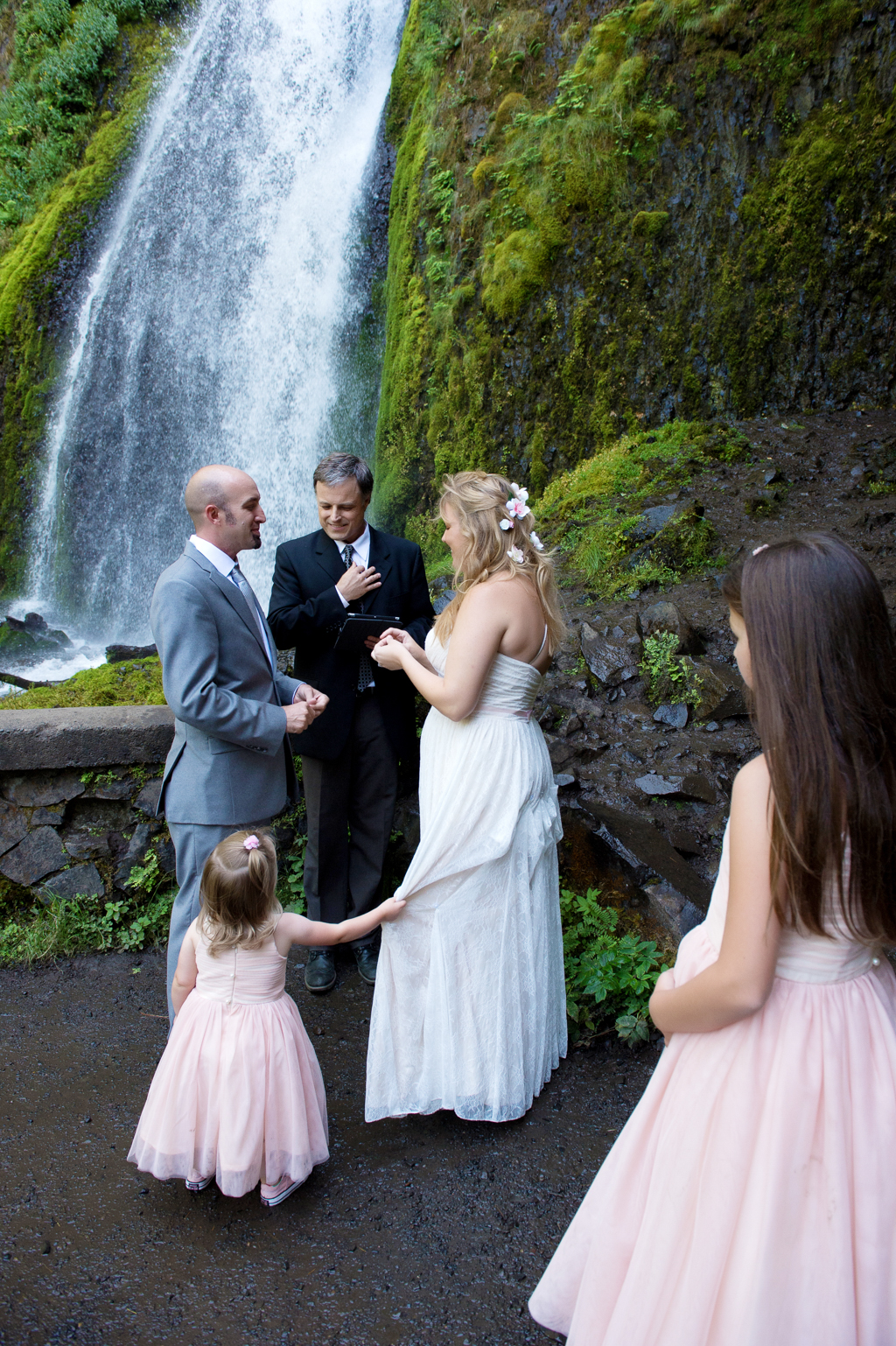 a little girl tugs on her mom's wedding dress during a wedding ceremony in front of wahkeena falls