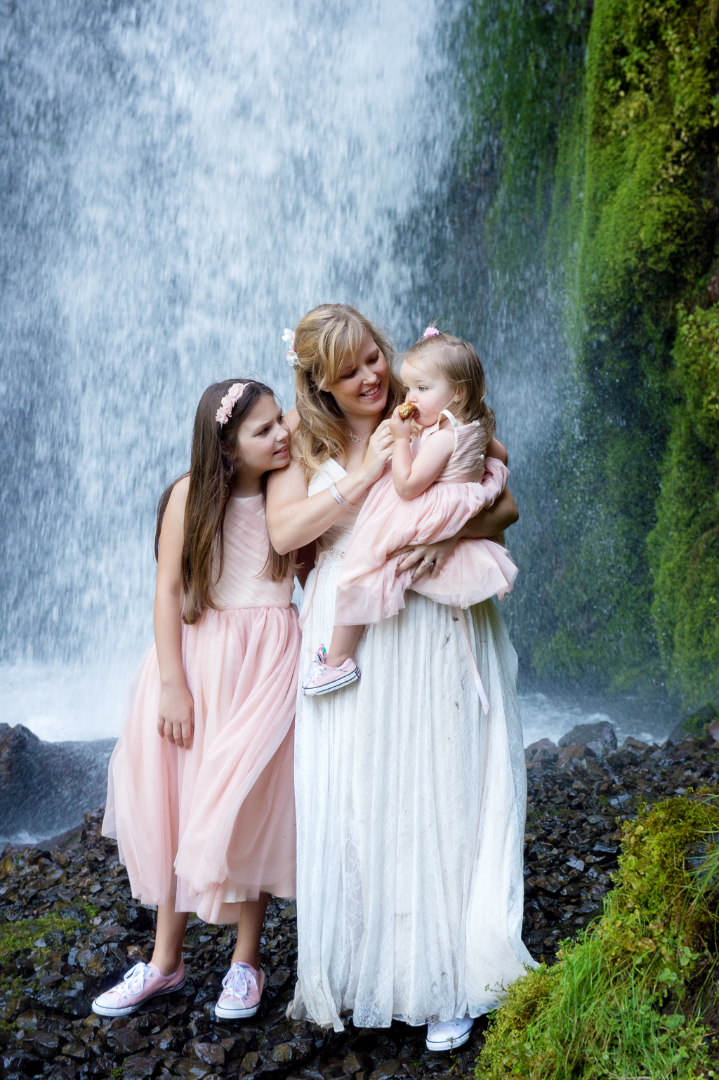 a mom bride  holds her baby daughter as her other daughter looks over her shoulder with wahkeena falls in the background