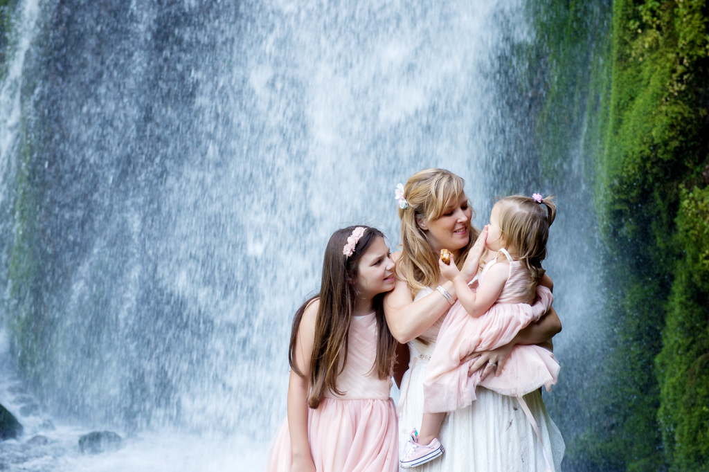 a mom bride  holds her baby daughter as her other daughter looks over her shoulder with wahkeena falls in the background