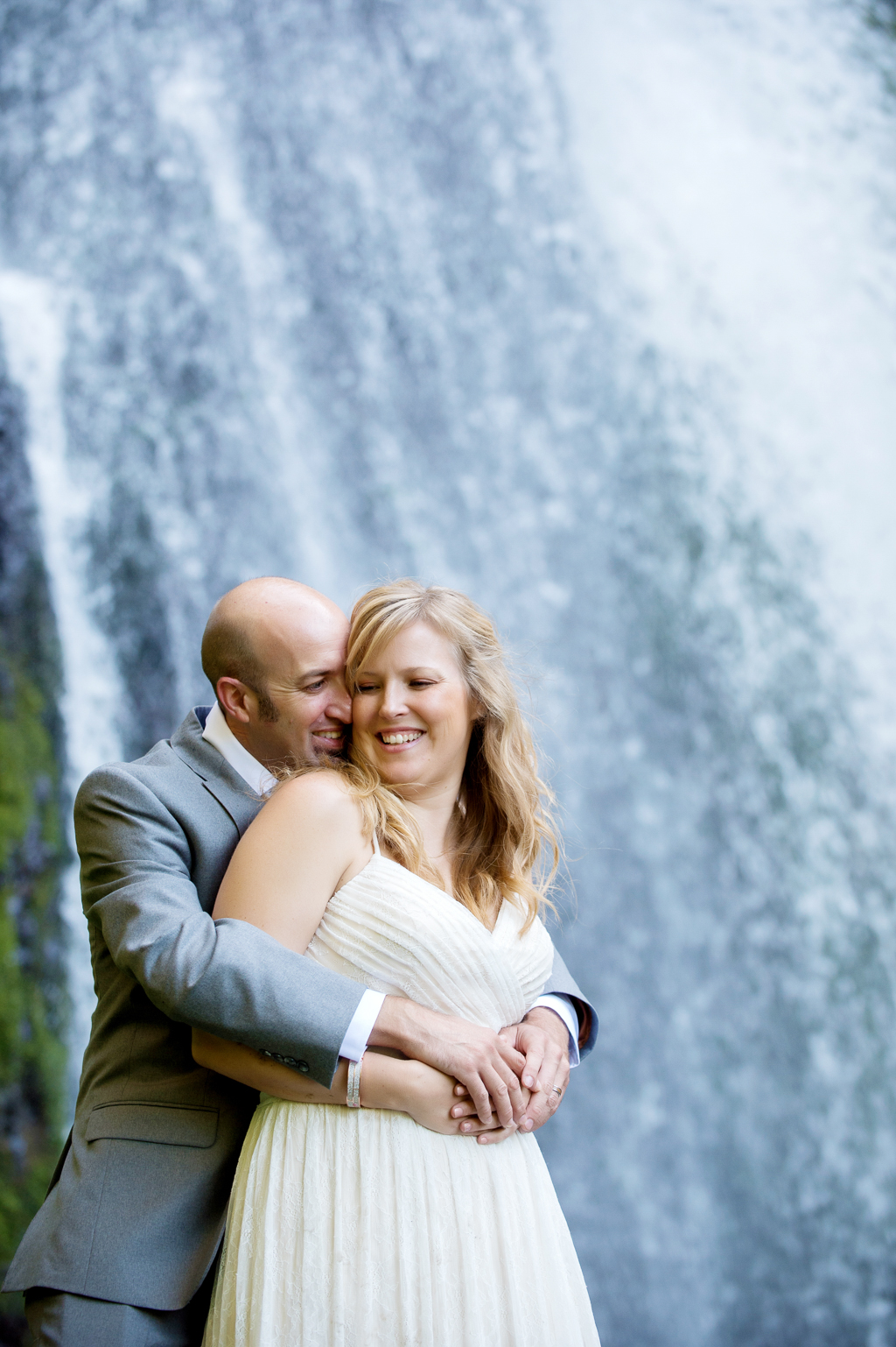 a groom hugs his bride from behind with a giant waterfall in the background