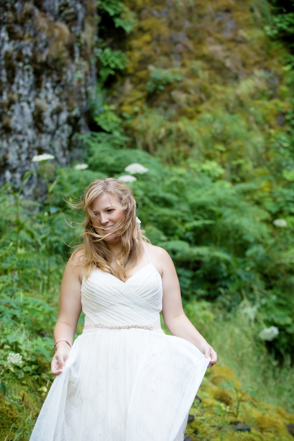 wind blows through a bride's hair as she stands in front of a mossy green cliff
