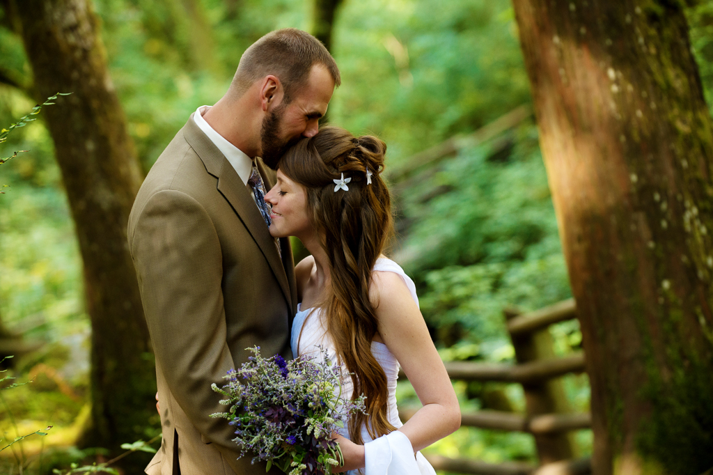 a groom kisses the top of a brides head in the forest at wallace falls