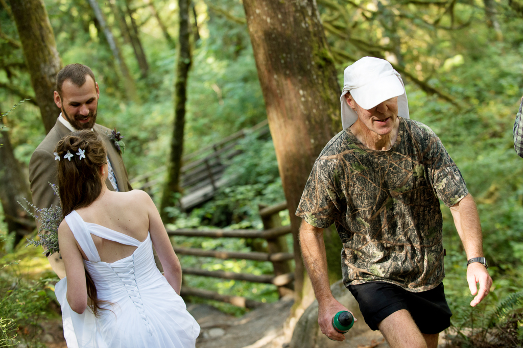 a bride and groom walk through the woods for their elopement as a hiker passes by