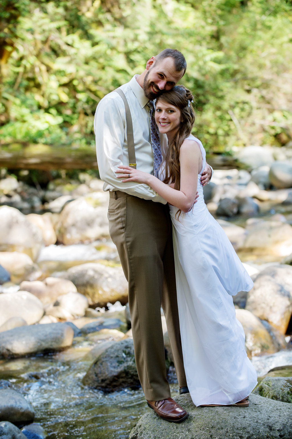 a bride and groom stand on a rock filled stream after their elopement in the forest