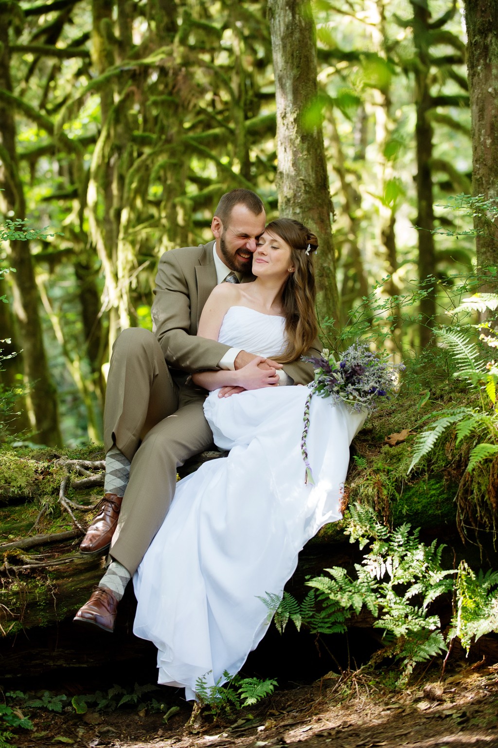a bride and groom sit on a log in the forest with their dog