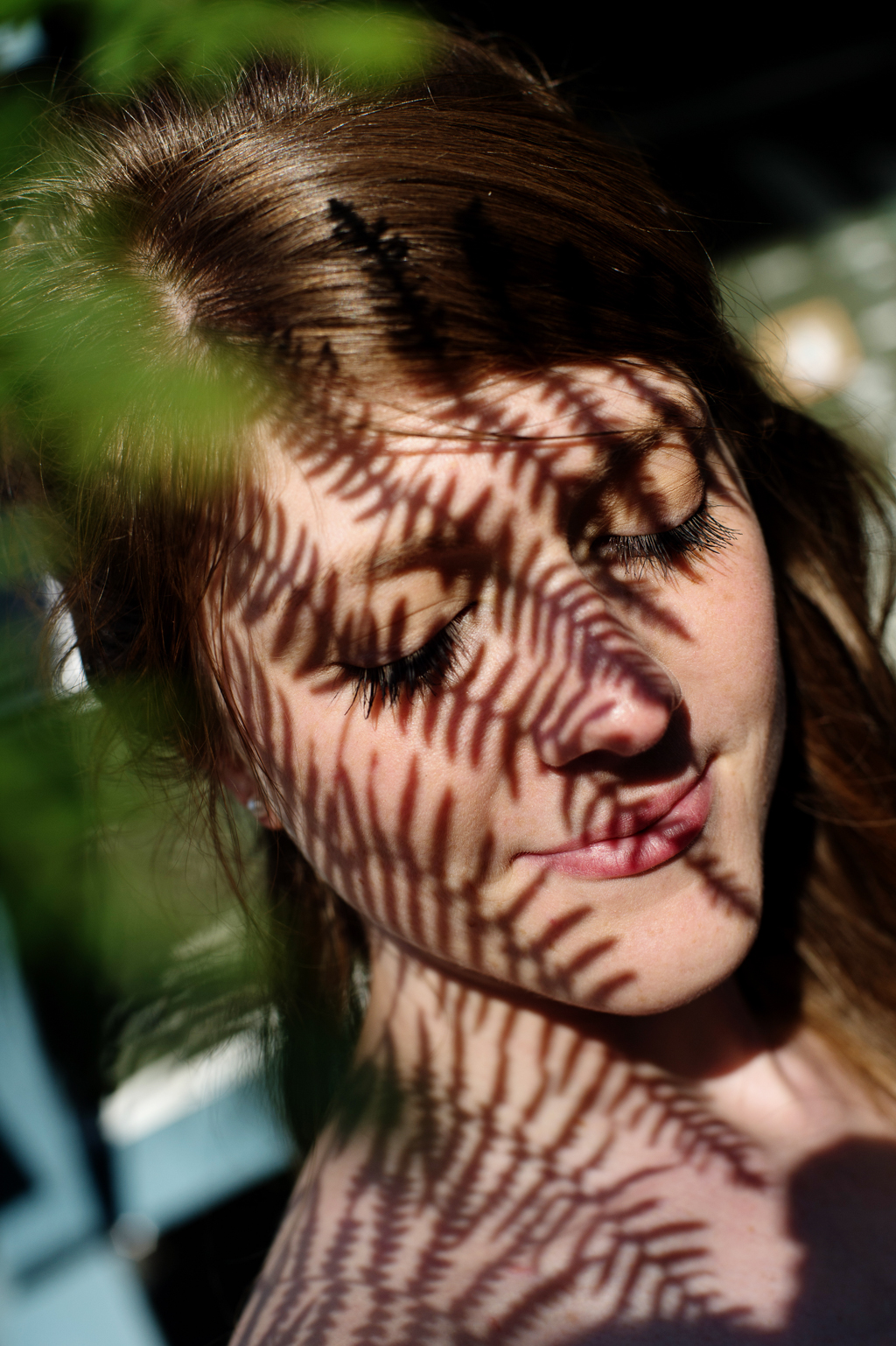 shadows from a fern leaf fall over a woman's face