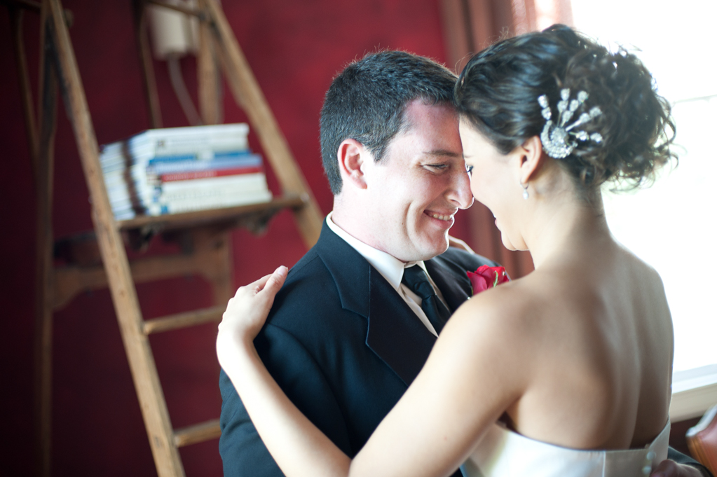 a bride and groom embrace in a dark red room in front of a wooden ladder that has books on it