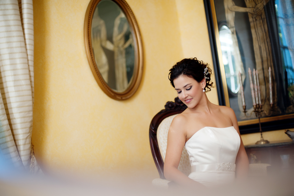 a bride sits in a vintage chair looking towards the floor in a yellow room with an antique oval portrait on the wall