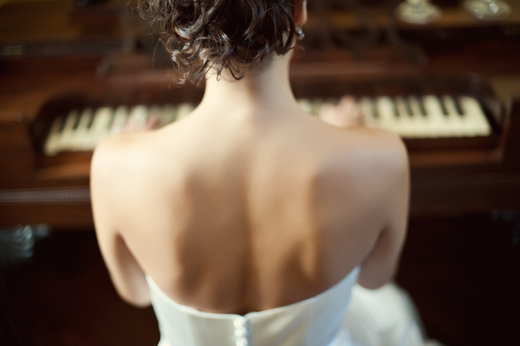 a bride's back as she sits playing piano