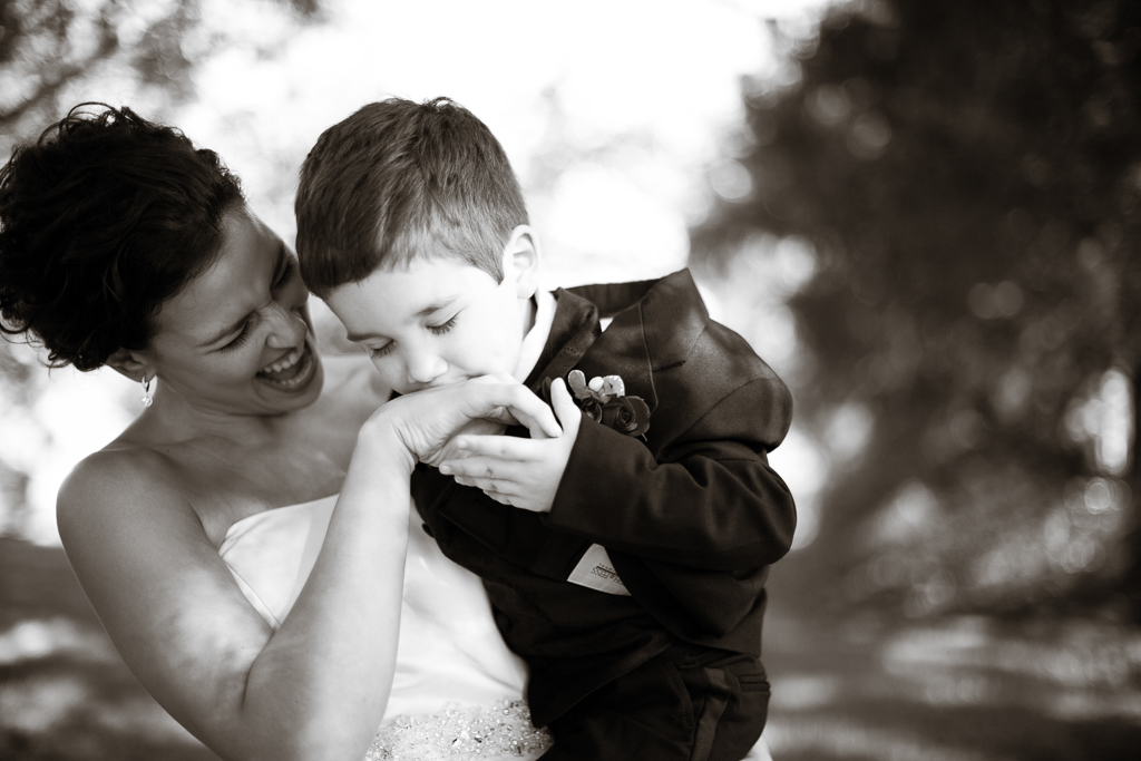 a bride holds a young boy in a suit as he kisses her hand