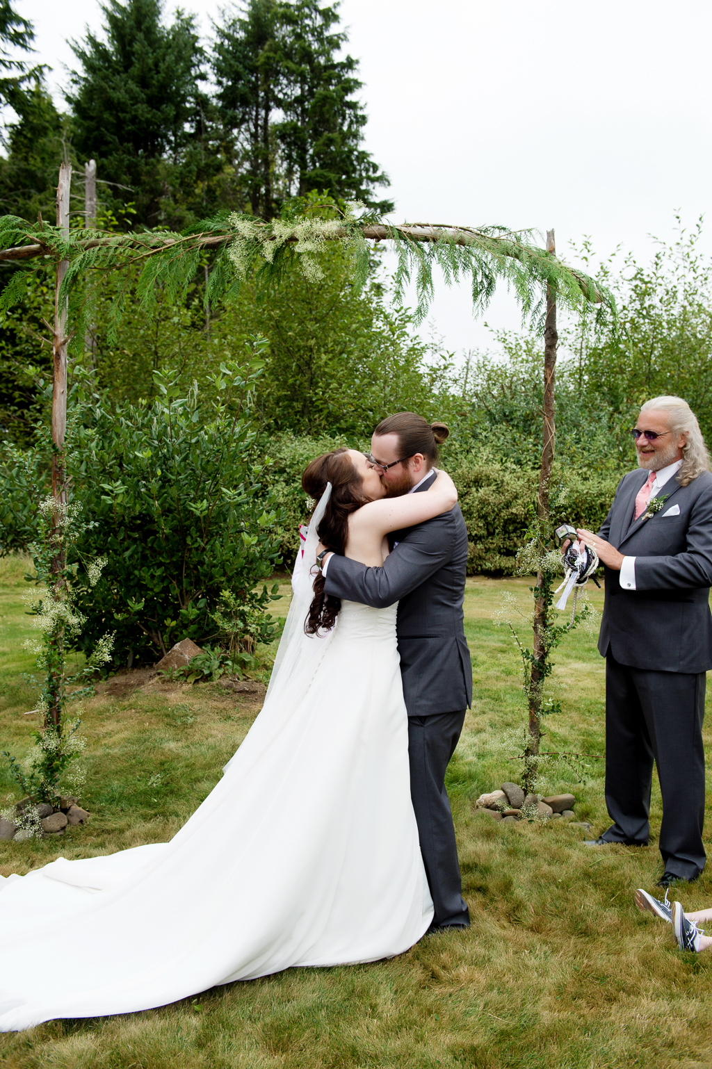 bride and groom have first kiss in front of fern covered arbor