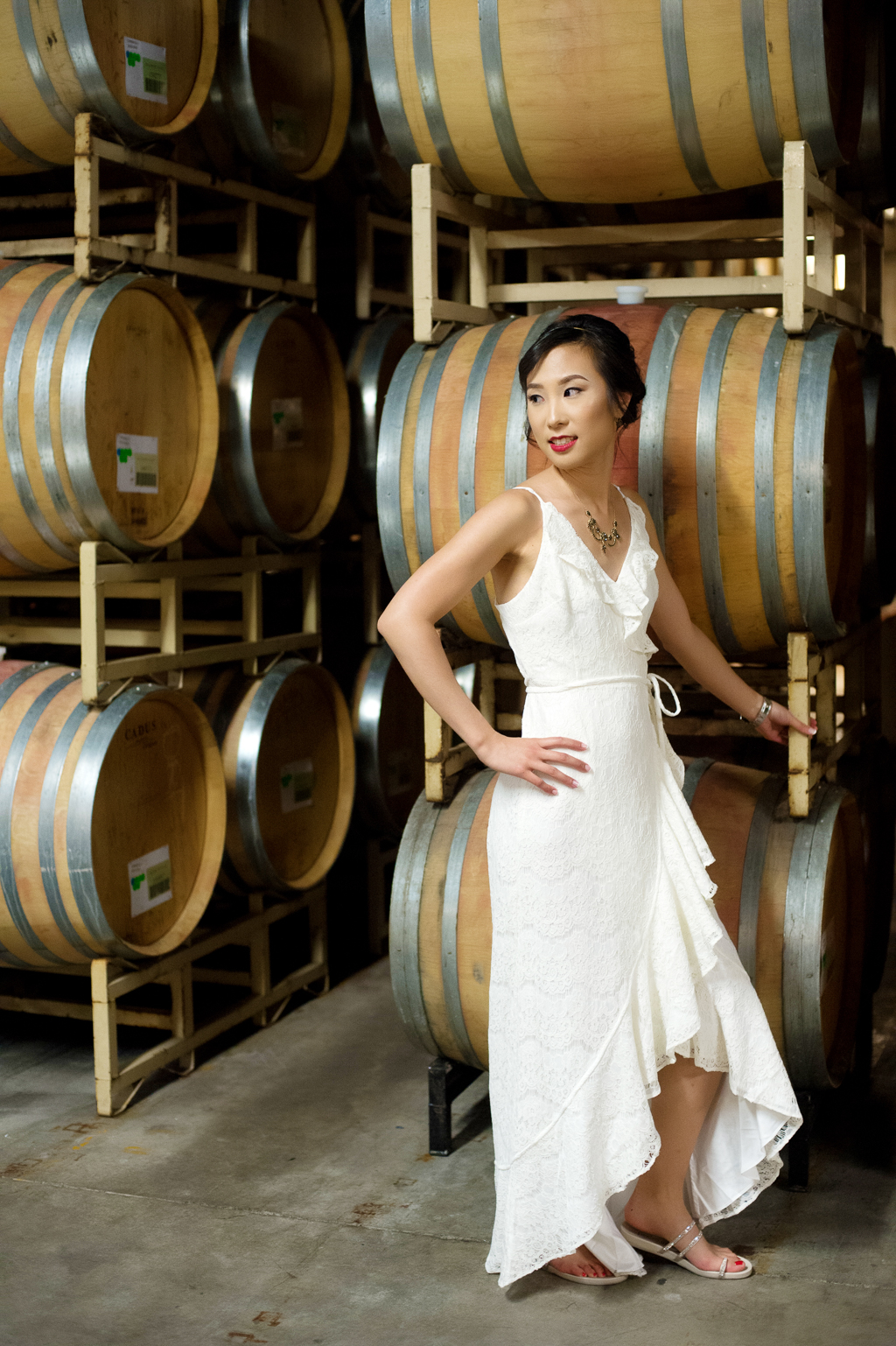 bride leans against wine barrels in the winery