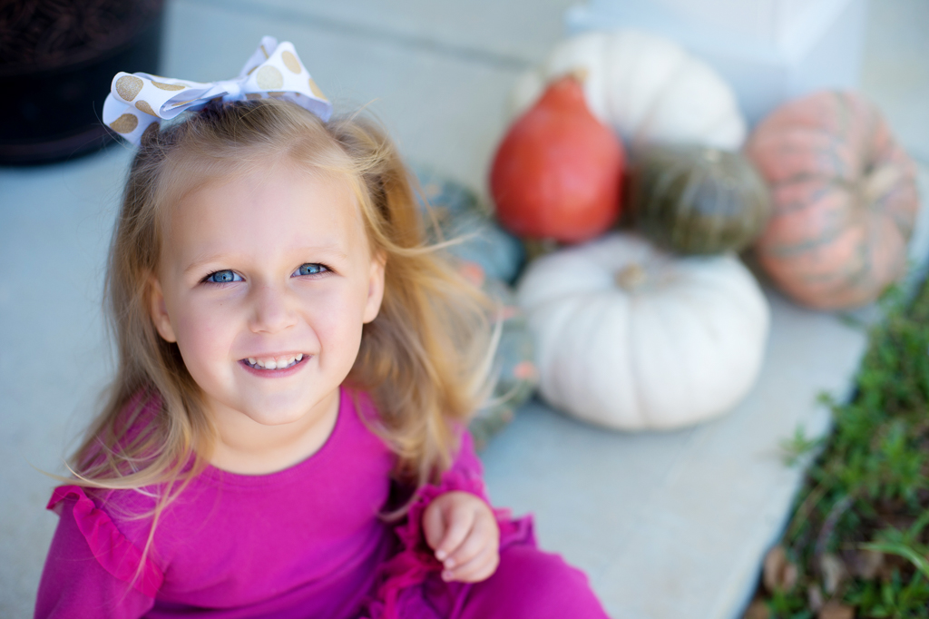 a young girl smiles sitting in front of multicolored pumpkins
