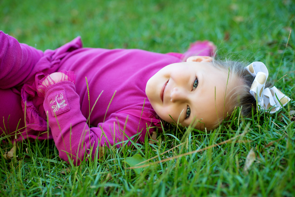 a young girl in hot pink lays in the grass and smiles 