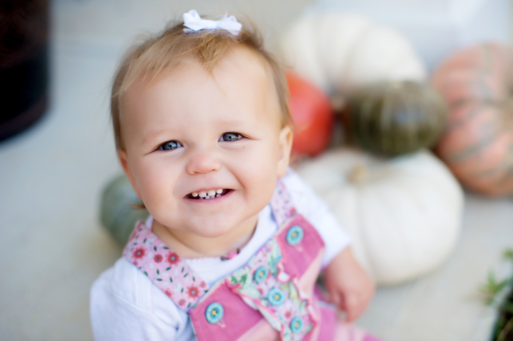 a baby girl smiles sitting in front of multicolored pumpkins