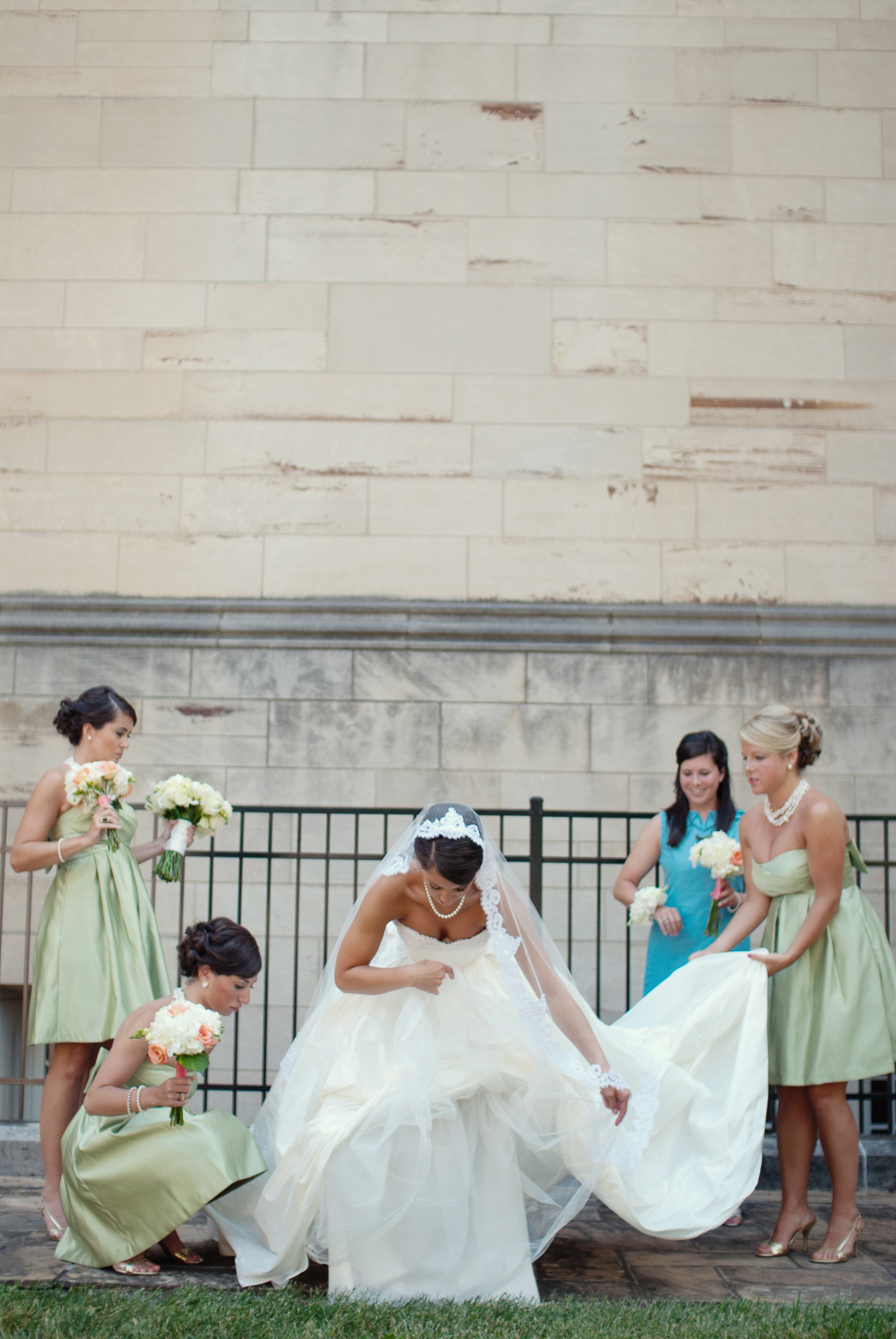 bridesmaids in green dresses help arrange bride's wedding dress