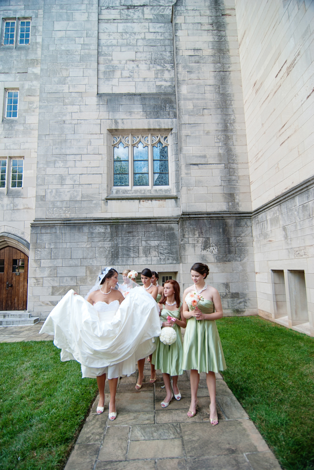 bride lifts giant wedding dress up as she walks with her bridesmaids outside the church