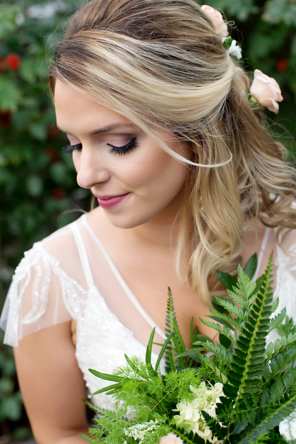 a bride has loose flowy wedding hair adorned with peach roses and holds a fern bouquet