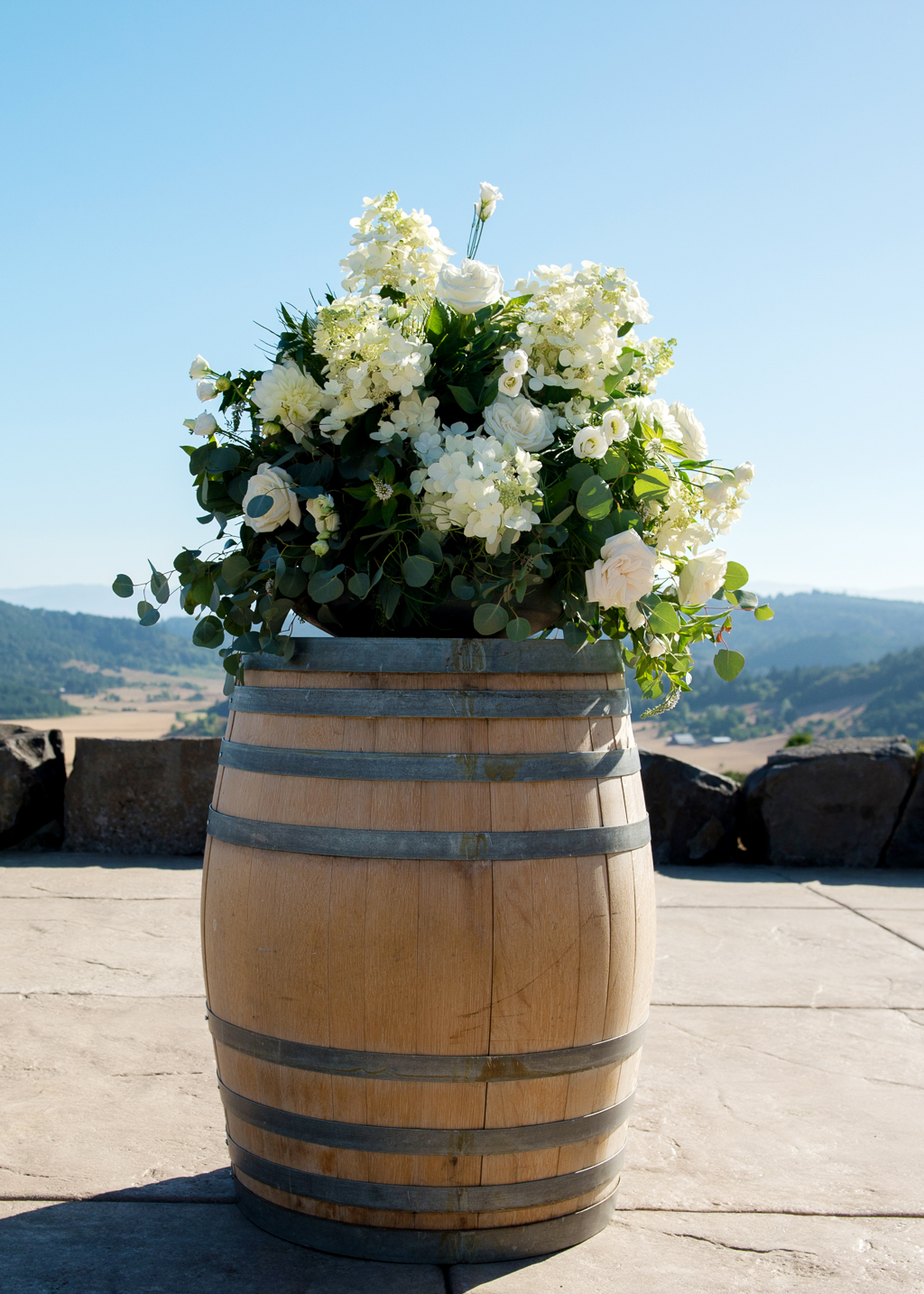 a large bouquet of ivory and white flowers sits atop a wine barrel at the front of the wedding ceremony