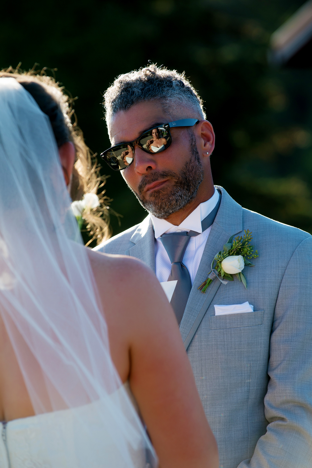 a brides reflection shows in the groom's sunglasses during their wedding vows