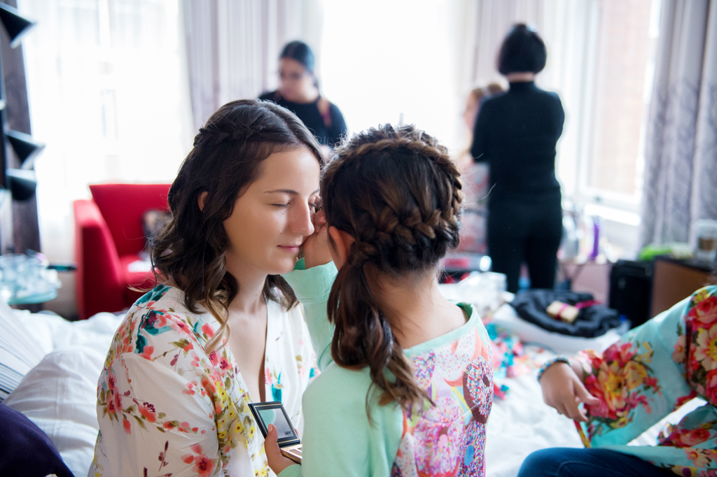 the young flower girl applies makeup to an older bridesmaid