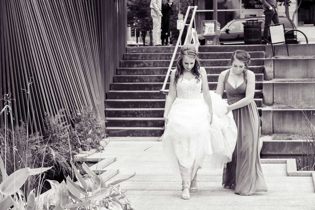 bridesmaid holds bride's wedding dress train up as she walks