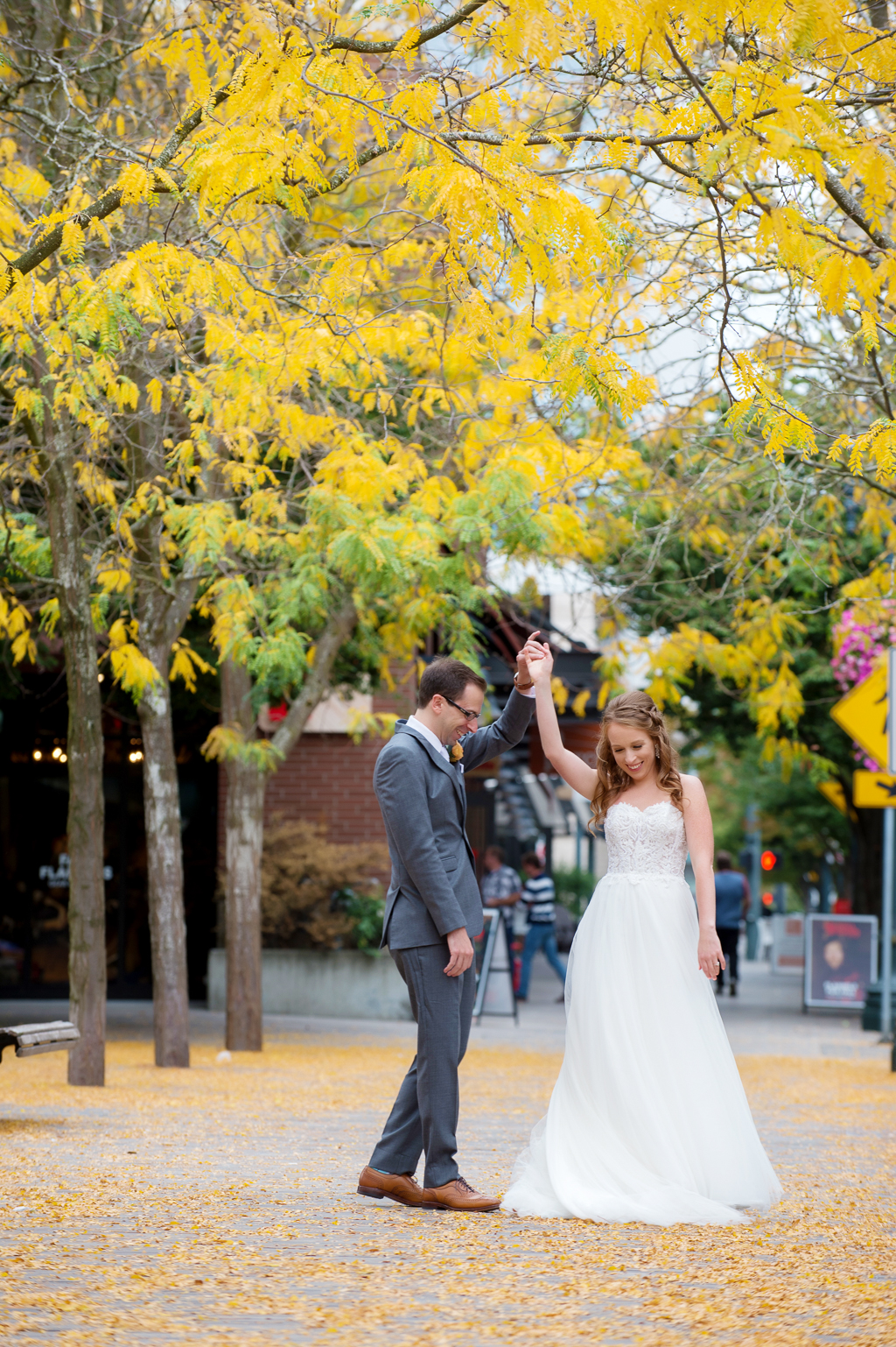 groom spins bride around in a pile of yellow leaves on the sidewalk in the pearl district