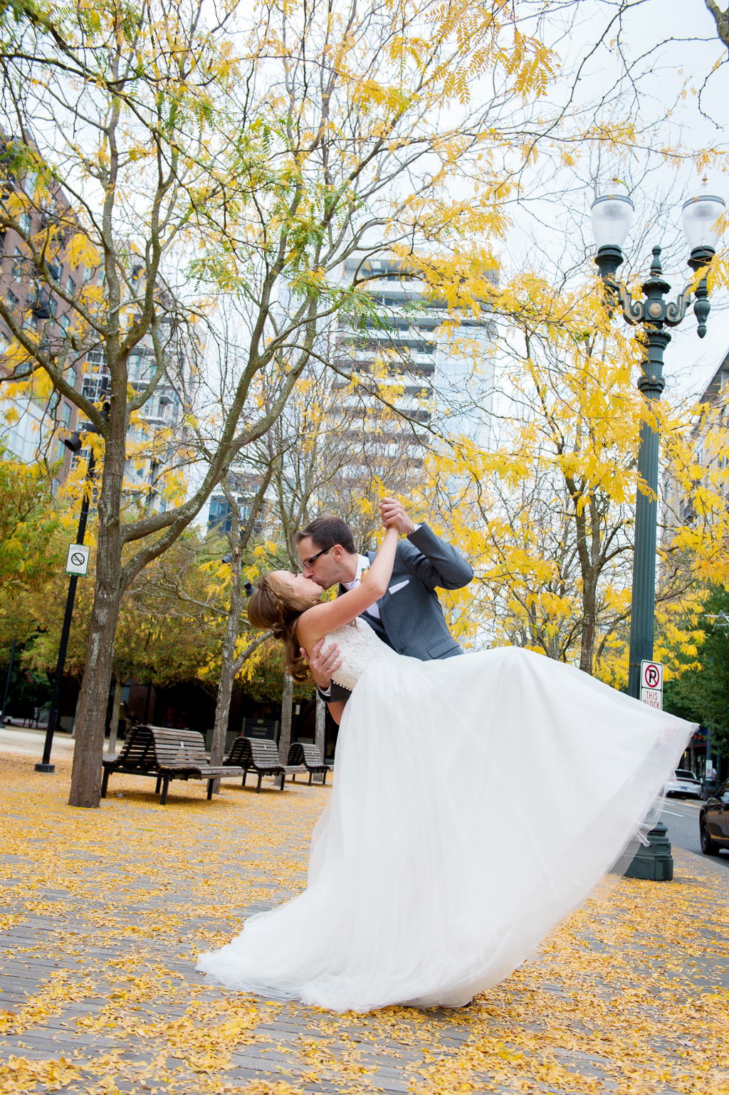 groom dips bride and kisses her on a sidewalk covered with yellow leaves in pearl district