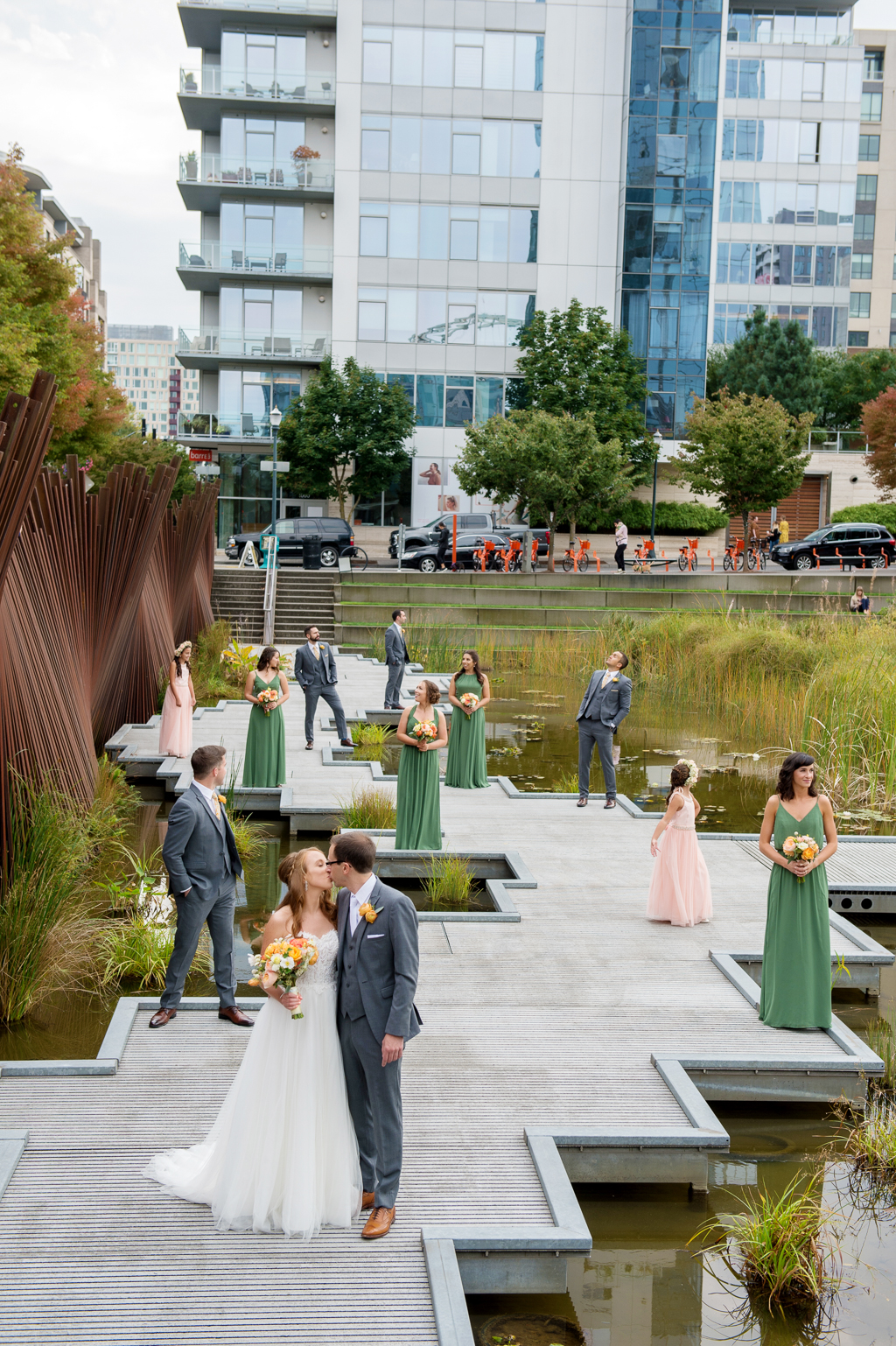 bridesmaids in green dresses and groomsmen line the boardwalk at tanner springs park